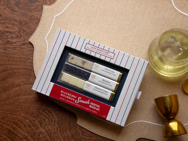 Blueberry Bourbon Smash cocktail mixer cubes in navy-and-stripe packaging beside a crafted bourbon cocktail.