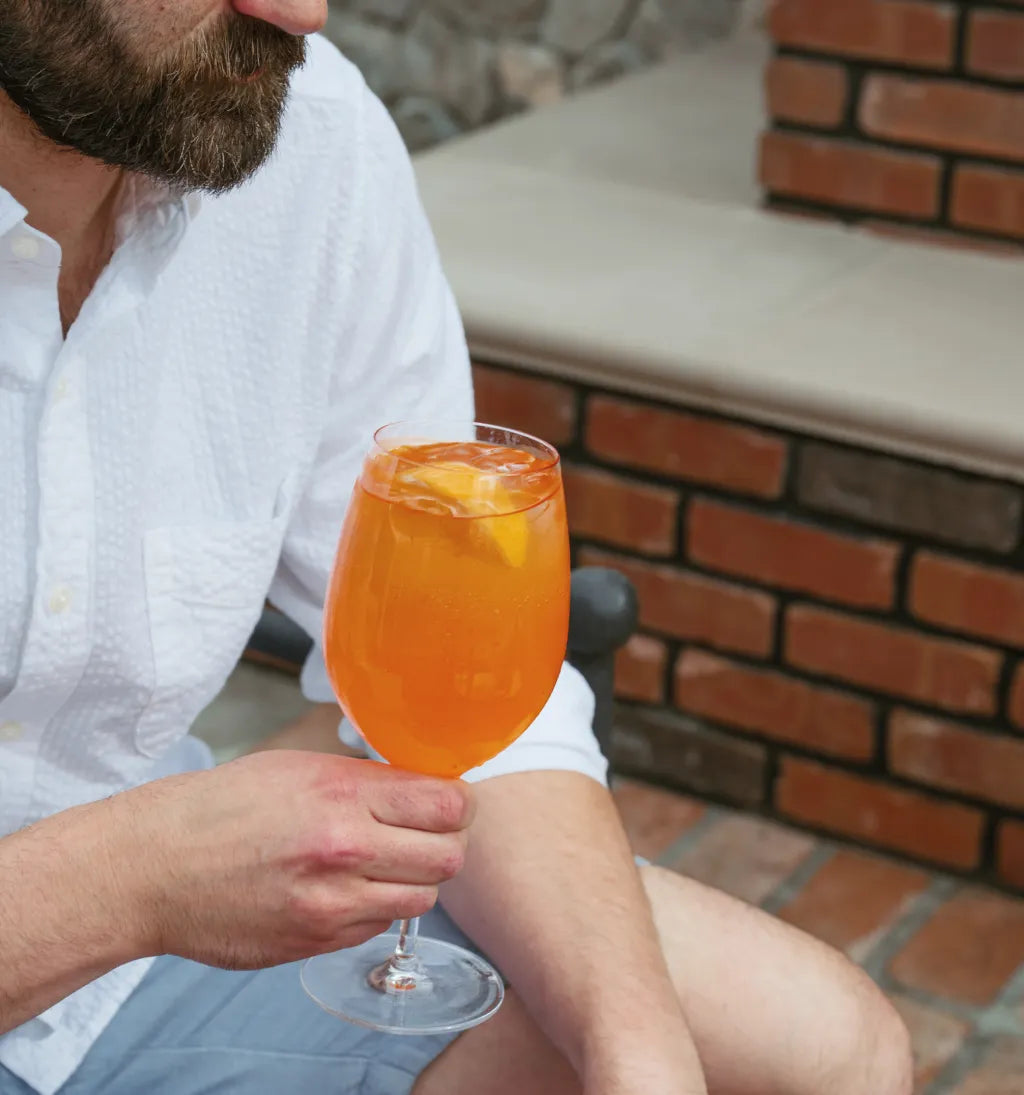 Man holding an aperitif spritz outdoors near a brick wall.