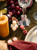 Wine glass with a decorative bow, candle, fruit, and cheese on a table.
