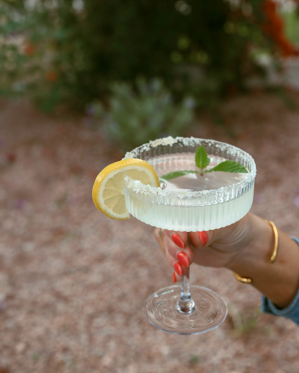 Cocktail with lemon wedge and mint leaf held by a hand outdoors