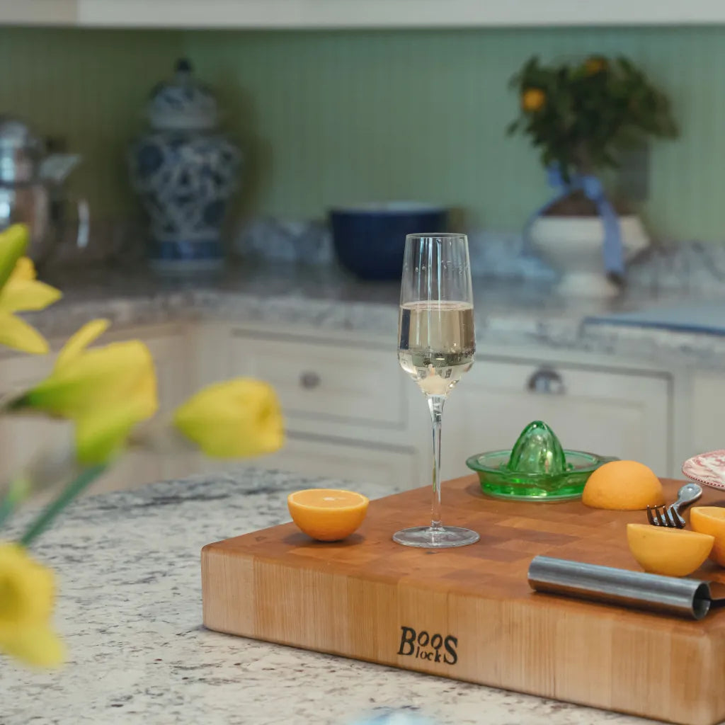 Glass of champagne on a cutting board with oranges and a juicer in a kitchen setting