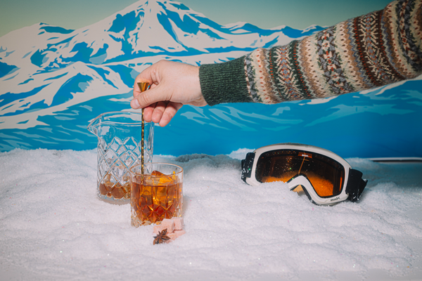 Person stirring an Old Fashioned into a glass with a snowy mountain background