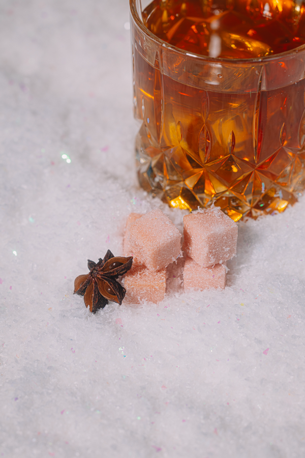 Glass of amber bourbon with star anise and Luxe Mixer Cubes on a snowy surface