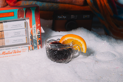 Hot mulled wine with orange slice in a mug, mulled wine box, and camera in the snow