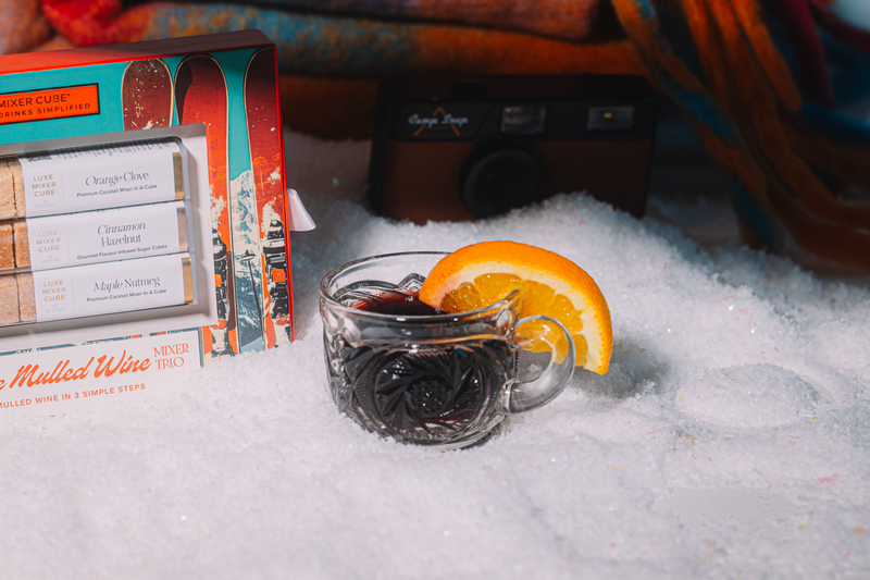 Hot mulled wine with orange slice in a mug, mulled wine box, and camera in the snow