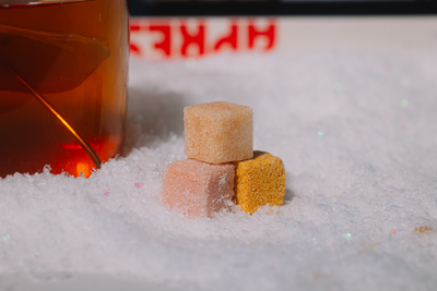 Three Luxe mixer cubes stacked on a snowy surface with a blurred bottle of alcohol in the background.