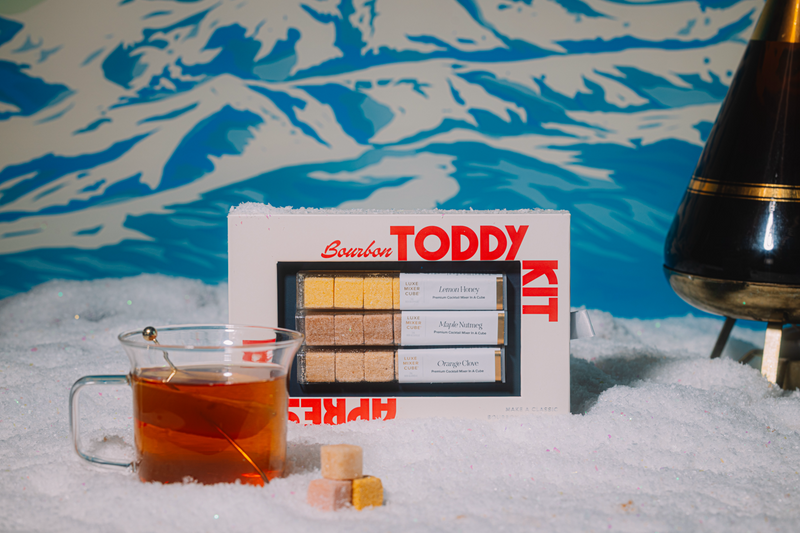 Bourbon Toddy Kit with a glass of amber liquid on a snowy background