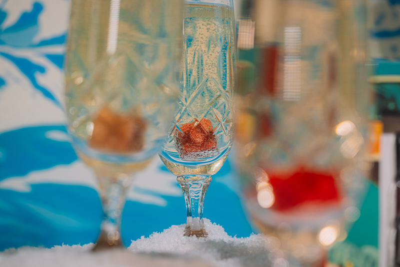 Close-up of a winter champagne glass with a Luxe Mixer Cube inside, set against a colorful winter background.