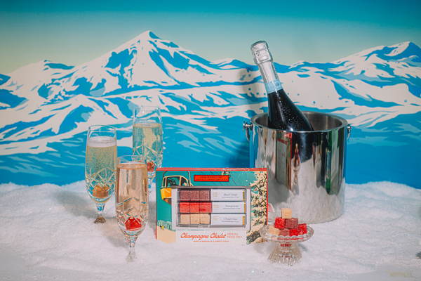 Bottle of champagne in an ice bucket with two glasses and a small tray or LUXE Mixer Cubes on a snowy mountain background