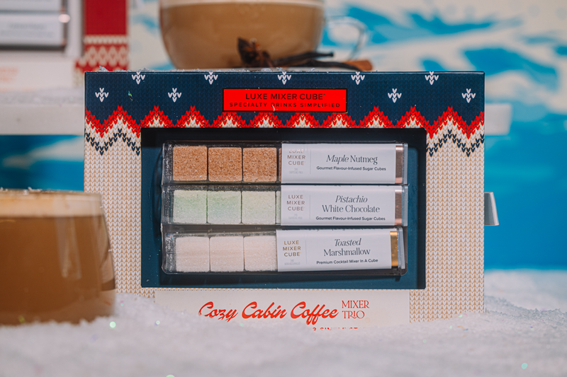Cozy Cabin Caffee mixer trio packaging with various flavors on a blurred background
