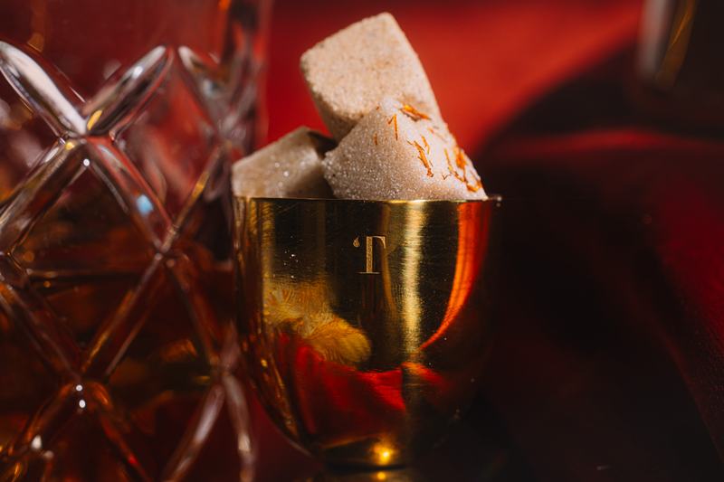 Gold Jigger filled with LUXE Mixer Cubes on a dark red background
