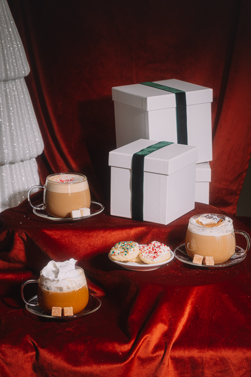 Two cups of coffee with whipped cream and cookies on a red surface with white gift boxes.