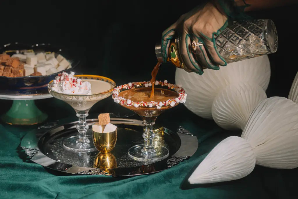 Cocktail being poured into a glass with decorative elements on a dark background