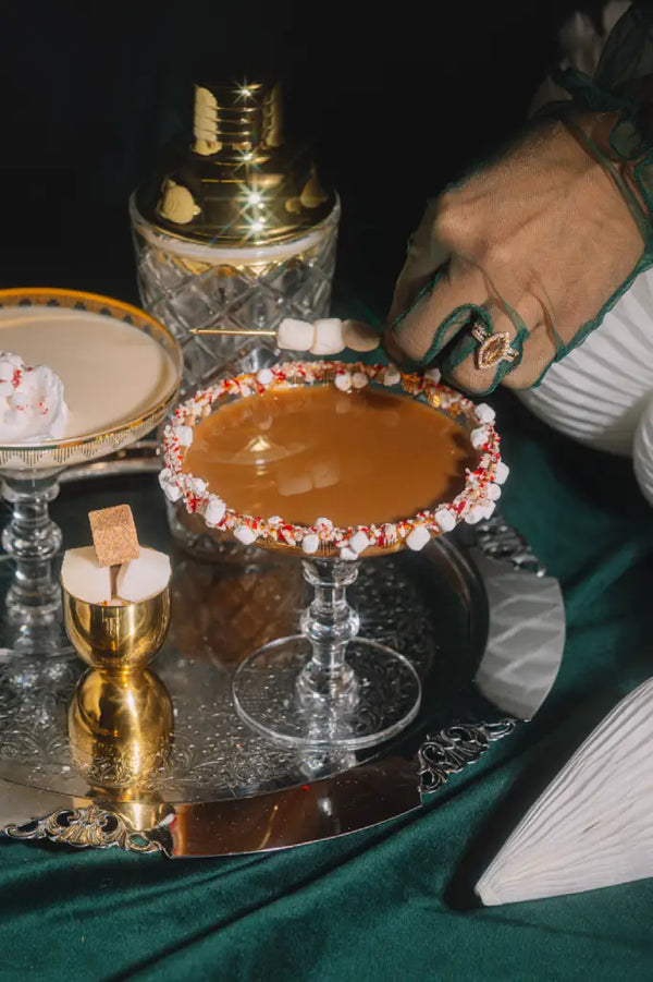 Cocktail with a rim decorated with candy on a tray, with a person's hand reaching towards it.