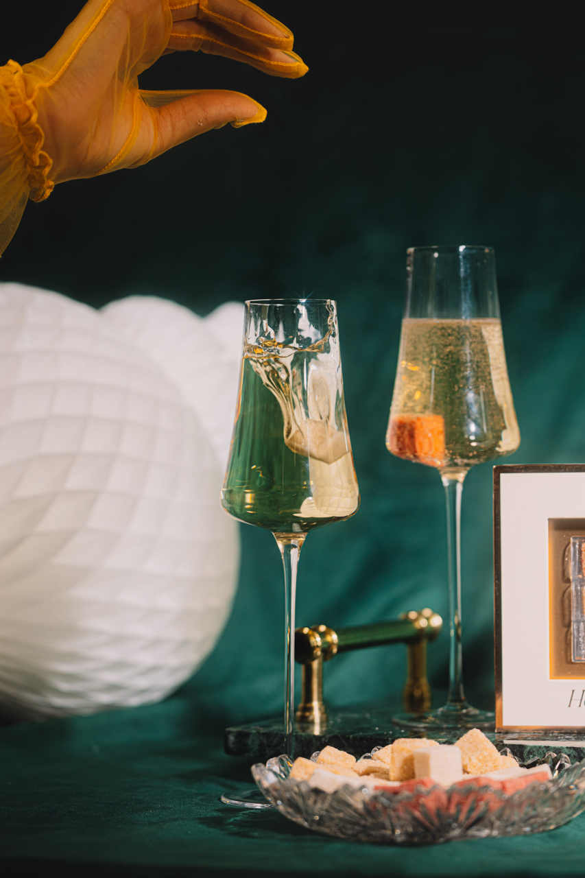 Two champagne glasses with a hand reaching towards them, set against a dark background.