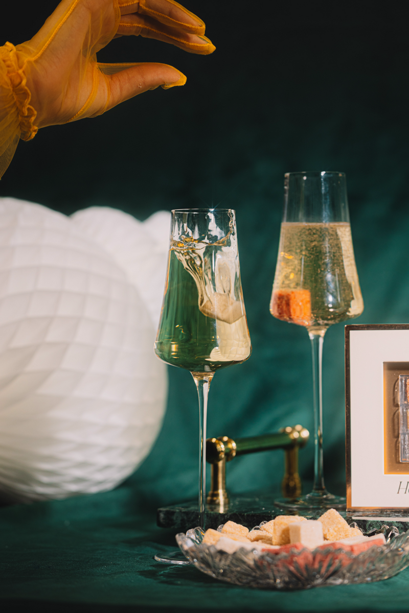 Two champagne glasses with a hand reaching towards them, set against a dark background.
