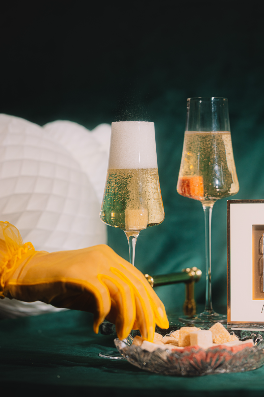 Two champagne flutes with bubbles, a yellow glove, and a framed picture on a dark surface.