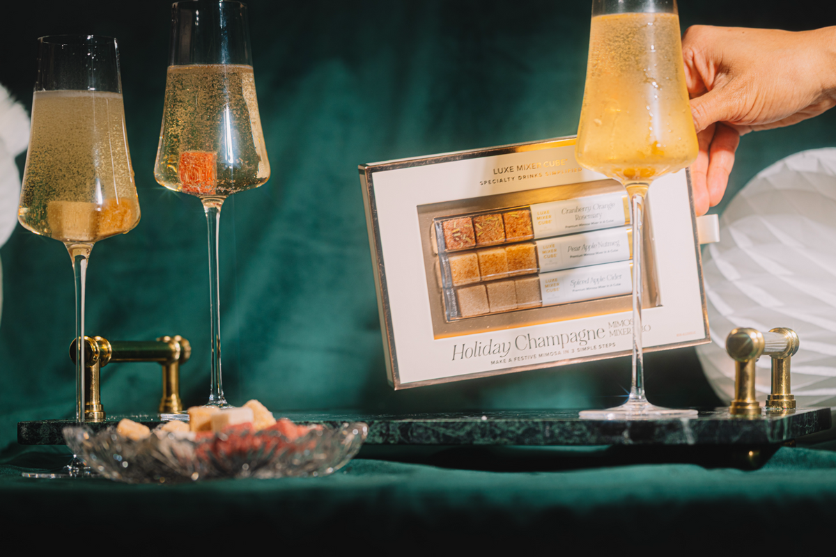 Two glasses of champagne on a tray with a box of chocolates, set against a dark green background.