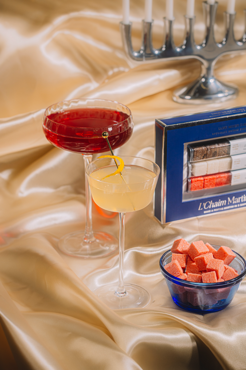 Two cocktails on a table with a box of L'Chaim Martinis and a bowl of watermelon cubes.