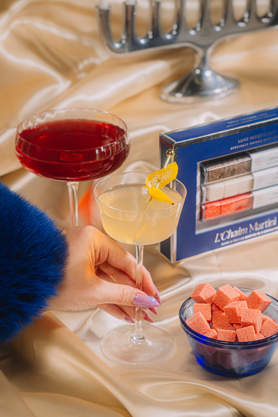 Two cocktails on a table with a box of matches and a bowl of pink cubes.