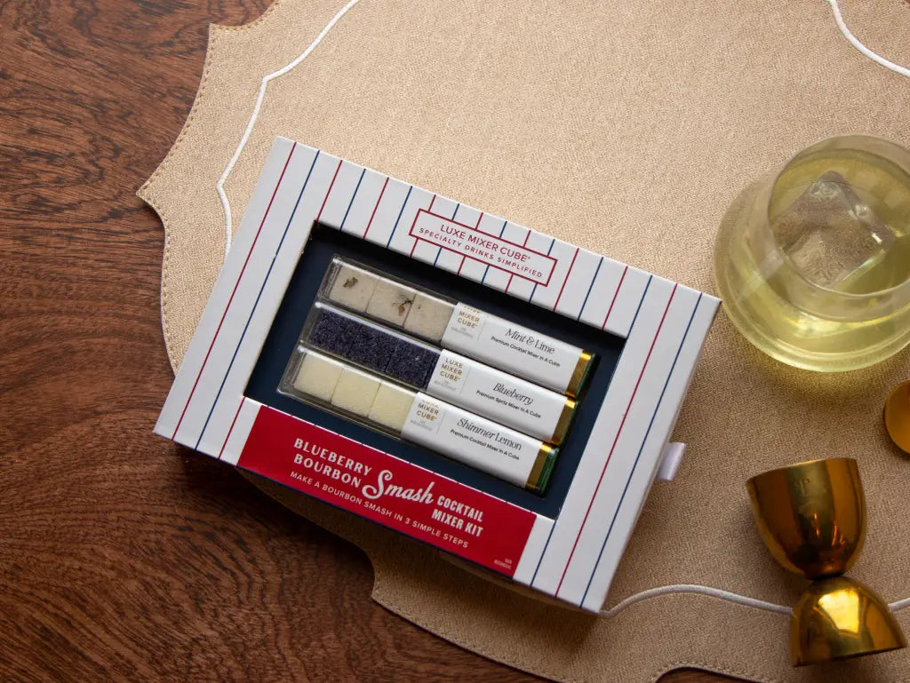 Blueberry Bourbon Smash cocktail mixer cubes in navy-and-stripe packaging beside a crafted bourbon cocktail.