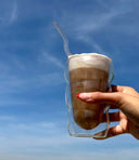 Hand holding a glass of iced coffee against a blue sky