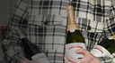 A person wearing a black and white plaid flannel shirt holds three bottles of champagne, with the center bottle clearly showing the brand name 'Cava Rossa' and the word 'CHAMPAGNE' on the label.