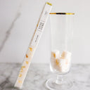 A tube of luxe sugar cubes with a gold accent, next to a clear glass containing sugar cubes.