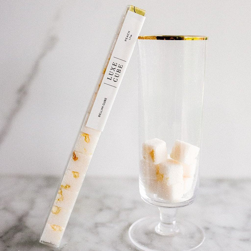 A tube of luxe sugar cubes with a gold accent, next to a clear glass containing sugar cubes.