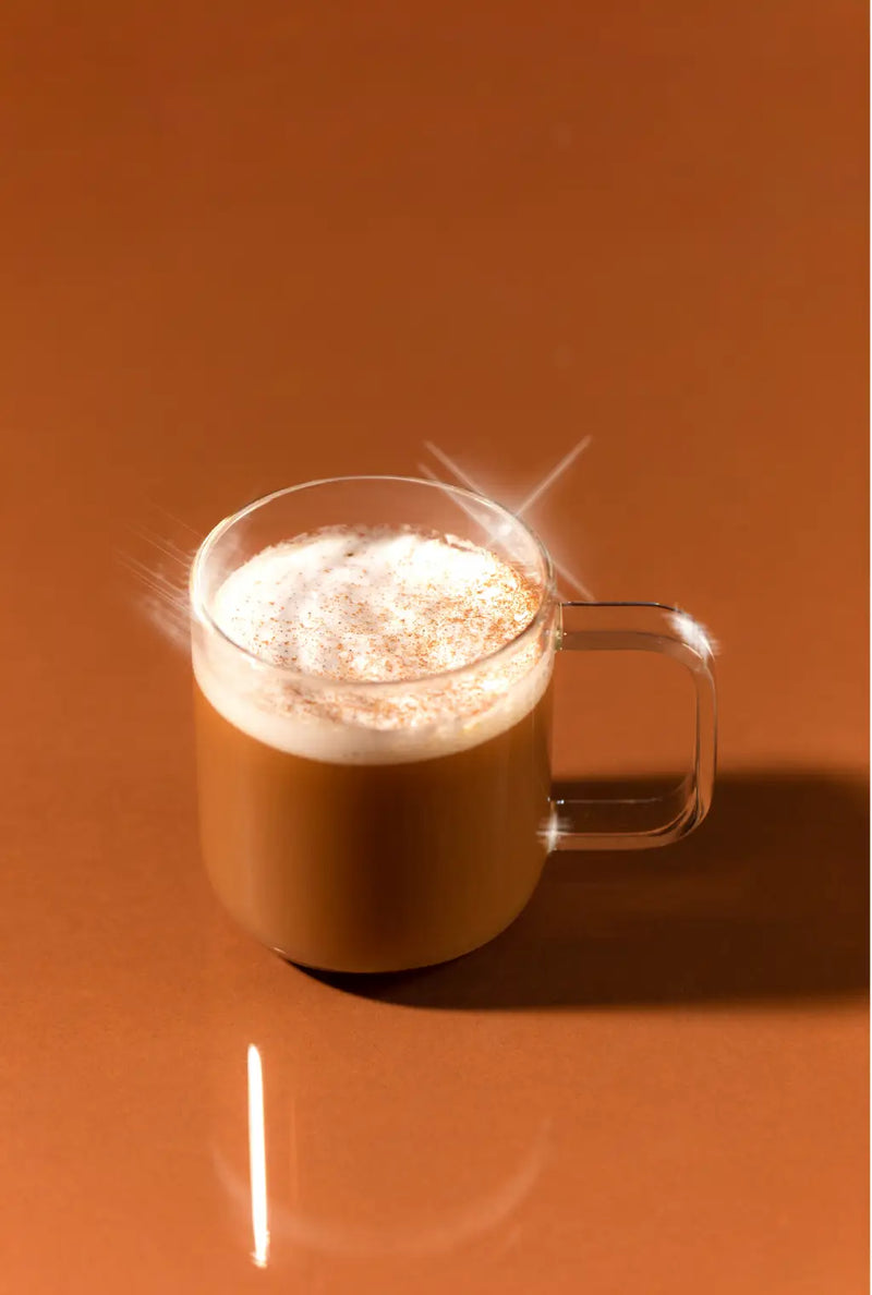 Glass mug of hot chocolate with a creamy top on a brown background